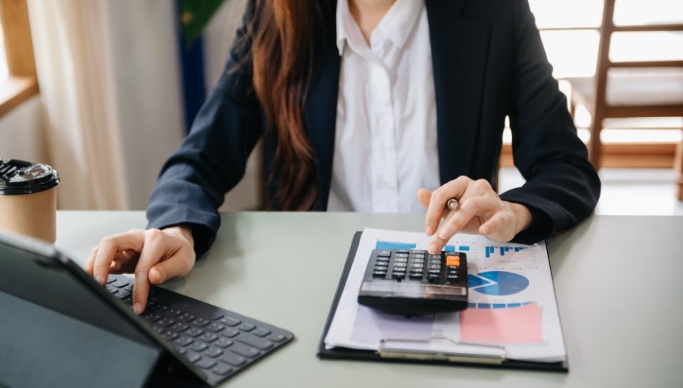 Woman hand business doing finances and calculate on desk about cost using on smartphone and tablet as concept